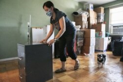 Joyce Lilly moves a filing cabinet as her dog Max follows, Tuesday, July 21, 2020, in the Riverdale neighborhood of The Bronx, in New York.