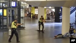 Dos policías holandeses apuntan sus armas hacia un hombre abatido a disparos por los agentes después de que éste apuñaló a dos personas en la estación central de trenes en Amsterdam, el viernes 31 de agosto de 2018. (AP Foto)