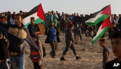 Protesters gather while others wave their national flags while near the fence of the Gaza Strip border with Israel during a protest on the beach near Beit Lahiya, northern Gaza Strip, Nov. 19, 2018.