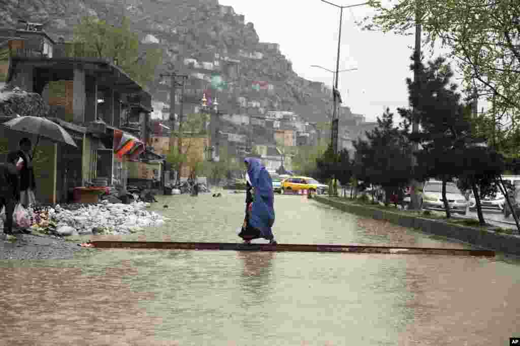 هنوز در شهر کابل برخی خیابان ها شاهد آب گرفتگی است و این زن سعی دارد از روی یک چوب عبور کند. در سیل افغانستان پنج نفر کشته و ۱۷ نفر ناپدید شدند.&nbsp;