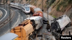 Sebuah kereta api penumpang melintasi kereta naas yang masih teronggok di sisi rel kereta api dekat stasiun di Santiago de Compostela, Spanyol Utara (27/7).