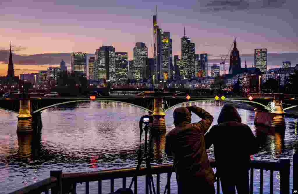 Two men take photographs of the buildings of the banking district in Frankfurt, Germany, after sunset.