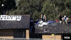 Lima orang tahanan duduk di atas atap salah satu bangunan di Pusat Penahanan Villawood di Sydney, Kamis (21/4). Mereka memasang tanda bertuliskan 'We Need Help' (Kami Butuh Pertolongan).