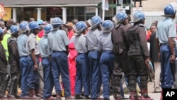 FILE: Zimbabwean police officers keep an eye on opposition party supporters as they prepare to march during a protest aimed at President Robert Mugabe in Harare, Zimbabwe, March, 14, 2016.