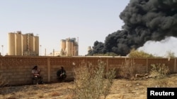 FILE - Members of forces loyal to Libya's eastern government sit near a factory during clashes with the Shura Council of Libyan Revolutionaries, an alliance of former anti-Gaddafi rebels who have joined forces with Islamist group Ansar al-Sharia.