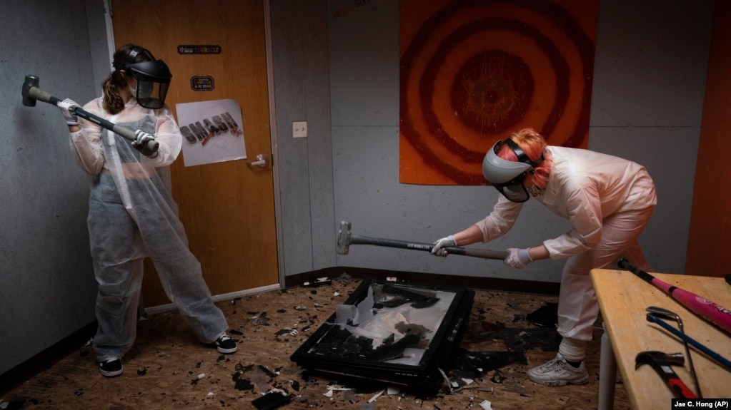 To release stress, Piper Mape, 17, right, and sister, Berkley, 15, use sledgehammers to destroy a TV in a rage room at Smash Rx in Westlake Village, California, February 5, 2021. (AP Photo/Jae C. Hong)