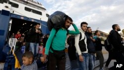 A man carries his belongings as other migrants and refugees arrive on a ferry from the Greek island of Lesbos at the Athens' port of Piraeus, Sept. 30, 2015. 