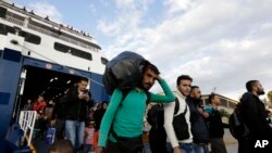 A man carries his belongings as other migrants and refugees arrive on a ferry from the Greek island of Lesbos at the Athens' port of Piraeus, Sept. 30, 2015.