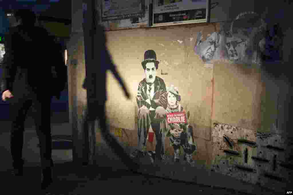 A man walks past a paper mural of actor Charlie Chaplin with the lettering 'We are Charlie' (Nous sommes Charlie) and portraits of Charlie Hebdo cartoonists Georges Wolinski, Stéphane Charbonnier in Paris on January 6, 2016.