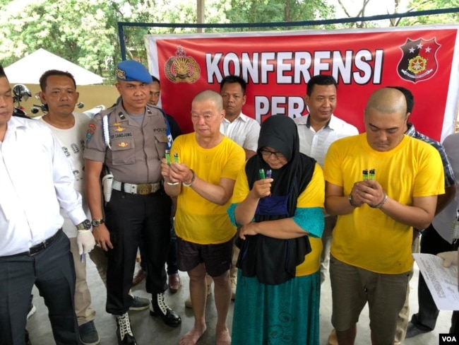 Polisi bersama ketiga tersangka (baju kuning) terbakarnya pabrik rumahan korek api gas di Langkat, Sumatera Utara, Indramawan (kiri), Lismawarni, dan Burhan, Senin (24/6). (VOA/Anugrah Andriansyah)