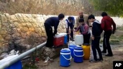 This frame grab from video provided By Yomyat Kzefeh Hawen Fi Dimashq (Diary of a Mortar Shell in Damascus), a Damascus-based media outlet that is consistent with independent AP reporting, shows Syrian residents filling up buckets and gallons of spring water from a pipe on the side of the road, in Damascus.