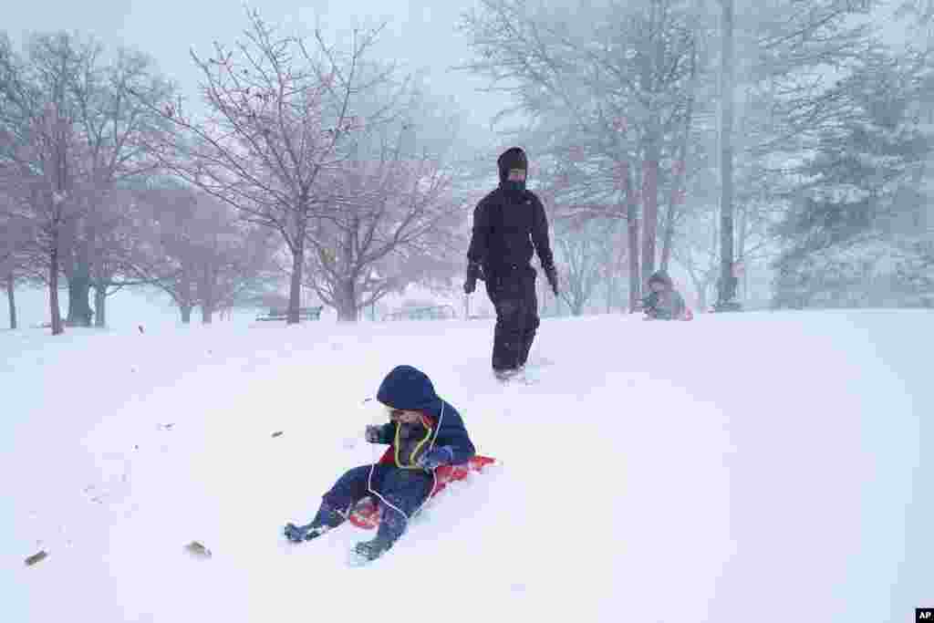 Liz Cote, center, watches as her son Ezra Crocombe, 4, left, attempts to sled down a hill as her other son Ori Crocombe, 1, looks on, in Baltimore, Maryland during a snowy day.