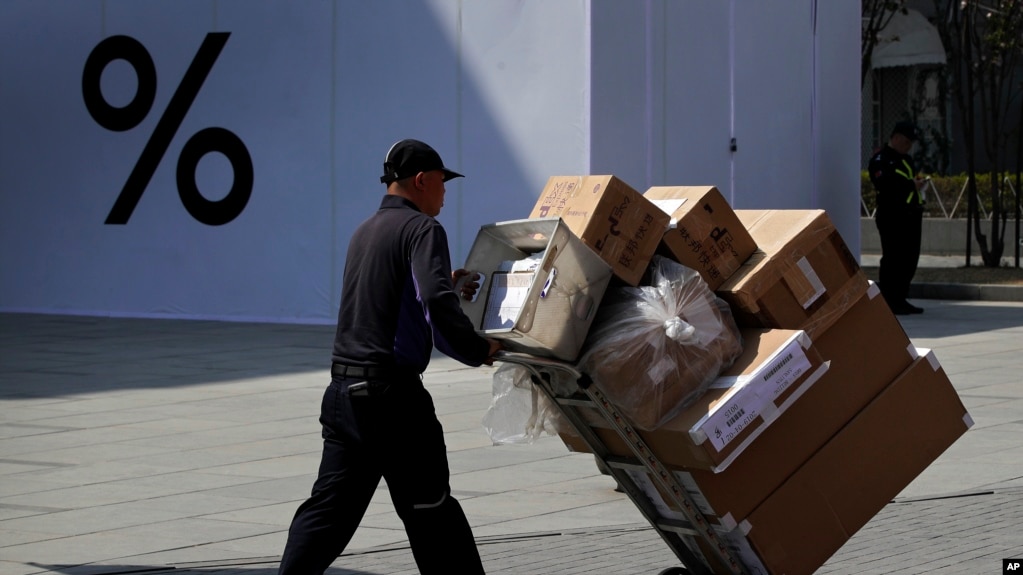 一个快递员推着载满货品的推车经过北京一个购物中心。(photo:VOA)
