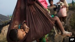 A Rohingya child is carried on a sling while his family walk through rice fields after crossing the border into Bangladesh near Cox's Bazar's Teknaf area, Sept. 5, 2017.