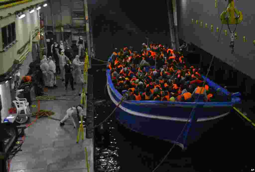 In this photo released by the Italian Navy, a fishing boat filled with migrants is towed into the Navy ship San Giorgio headed to Sicily.