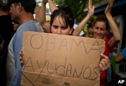 FILE - A Cuban migrant holds a sign that reads in Spanish "Help us Obama" during a protest at the Costa Rican border with Nicaragua, Nov. 16, 2015.