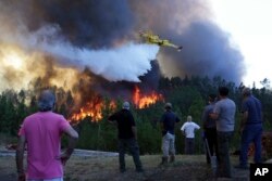 Villagers watch a firefighting plane drop water to stop a raging forest fire reaching their houses just a few dozen meters away in the village of Chao de Codes, near Macao, central Portugal.
