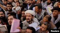 Afghans gather outside the passport office after Taliban officials announced they will start issuing passports to its citizens again, following delays that hampered attempts by those trying to flee the country after the Taliban seized control, in Kabul, A