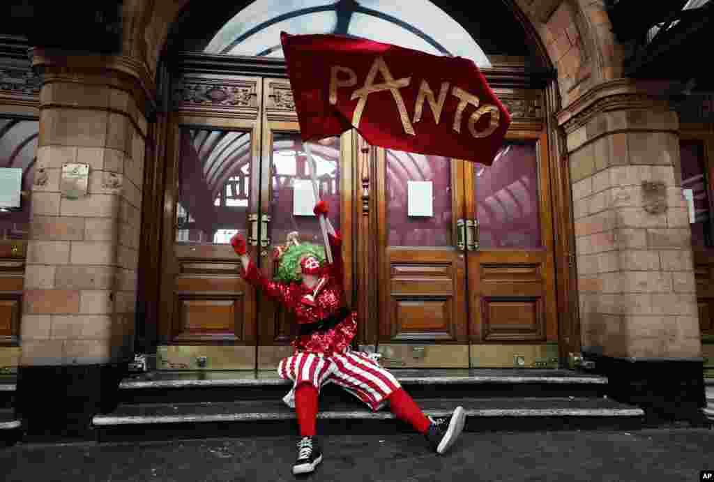 An actor dressed as pantomime dame waves a flag at the entrance of a theater before marching on Parliament to demand more support for the theater sector amid the COVID-19 pandemic, in London.