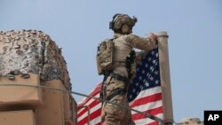 American soldier mount the U.S. flag on a vehicle near the town of Tel Tamr, north Syria, Sunday, Oct. 20, 2019. 