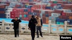 FILE - Security guards walk in front of containers at the Yangshan Deep Water Port in Shanghai, April 24, 2018.