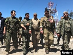 FILE - A U.S. military commander, second from right, walks with Kurdish fighters from the People's Protection Units (YPG) at the YPG headquarters that was hit by Turkish airstrikes in Mount Karachok near Malikiya, Syria, April 25, 2017.