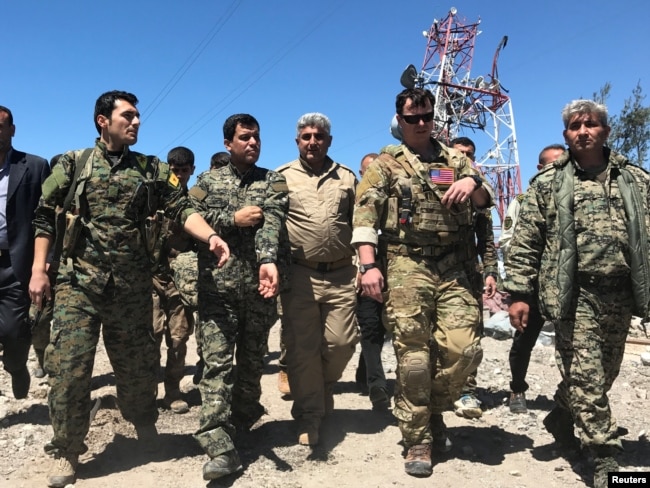 FILE - A U.S. military commander, second from right, walks with Kurdish fighters from the People's Protection Units (YPG) at Mount Karachok near Malikiya, Syria, April 25, 2017.