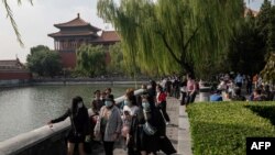 Para wisatawan mengenakan masker sebagai tindakan pencegahan terhadap virus Covid-19 saat berjalan-jalan di sekitar Kota Terlarang (latar belakang) selama hari nasional yang menandai hari libur nasional "Pekan Emas" di Beijing, 1 Oktober 2020. 