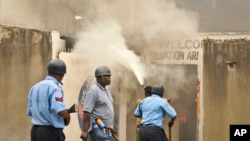 Policeman armed with pistol and tear gas patrols while firemen extinguish fire set by rioting youth at Salvation Army Church, Mombasa, Kenya, Oct. 4, 2013.