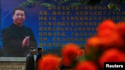 Men walk past a poster of the Chinese People's Liberation Army (PLA) featuring a portrait of President Xi Jinping, on the second day of plenary sessions of the 18th Central Committee of the Communist Party of China (CPC) in Beijing, Oct. 25, 2016.