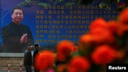 FILE - Men walk past a poster of the Chinese People's Liberation Army (PLA) featuring a portrait of President Xi Jinping, on the second day of plenary sessions of the 18th Central Committee of the Communist Party of China (CPC) in Beijing, Oct. 25, 2016.