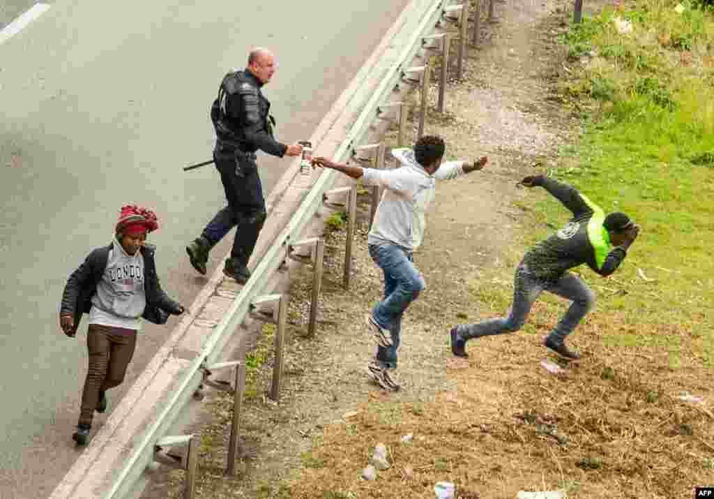 A police officer sprays tear gas at migrants trying to access the Channel Tunnel entrance on the A16 Highway in Calais, northern France.