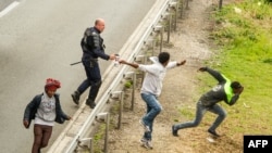 Police officer sprays tear gas at migrants trying to access Channel Tunnel on the A16 highway in Calais, northern France, June 23, 2015.