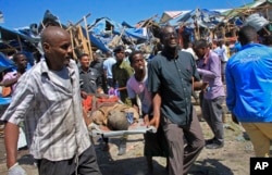 Somali men retrieve the dead body of a person who was killed when a car bomb targeted a police station in the Waberi neighborhood, where President Hassan Sheikh Mohamud was visiting a university, in the capital Mogadishu, Saturday, Nov. 26, 2016.