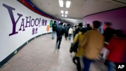 FILE - Chinese subway riders walk past a Yahoo advertisement at a metro station in Beijing.