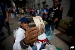 A street vendor inspects the authenticity of a 100-bolivar note as people stand in line outside a bank to deposit their bank 100-bolivar bank notes, in Caracas, Venezuela, Dec. 13, 2016.