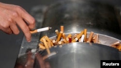 A man flicks ashes from his cigarette over a dustbin in Shanghai January 10, 2014. 