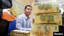 FILE - Stacks of 100,000 Vietnamese Dong notes ($4.70) are pictured as employees count money at a branch of the Bank for Investment and Development of Vietnam (BIDV) in Hanoi.