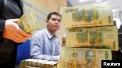 FILE - Stacks of 100,000 Vietnamese Dong notes ($4.70) are pictured as employees count money at a branch of the Bank for Investment and Development of Vietnam (BIDV) in Hanoi, Jan. 20, 2014. 