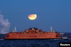 The "Super Blue Blood Moon" sets behind the Staten Island Ferry, seen from Brooklyn, New York, Jan. 31, 2018.