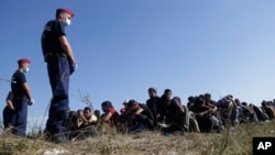 FILE - A group of migrants sits and waits to be escorted to a train after crossing a border from Croatia near the village of Zakany, Hungary, Sept. 23, 2015. Germany's interior minister expects the EU executive to propose new rules for protecting the bloc's frontiers that would mean European border guards stepping in when a national government failed to defend them.