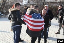 A male protester drapes himself with an American flag, Jan. 9, 2016. Many Kosovars still hold the United States in high regard after it led NATO airstrikes in 1999, which eventually helped the country gain independence from Serbia. (P.W. Wellman/VOA)
