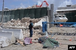 A Somali soldier stands next to a crumbled perimeter wall outside the UN's office in Mogadishu on July 26, 2016 following twin car bombings.