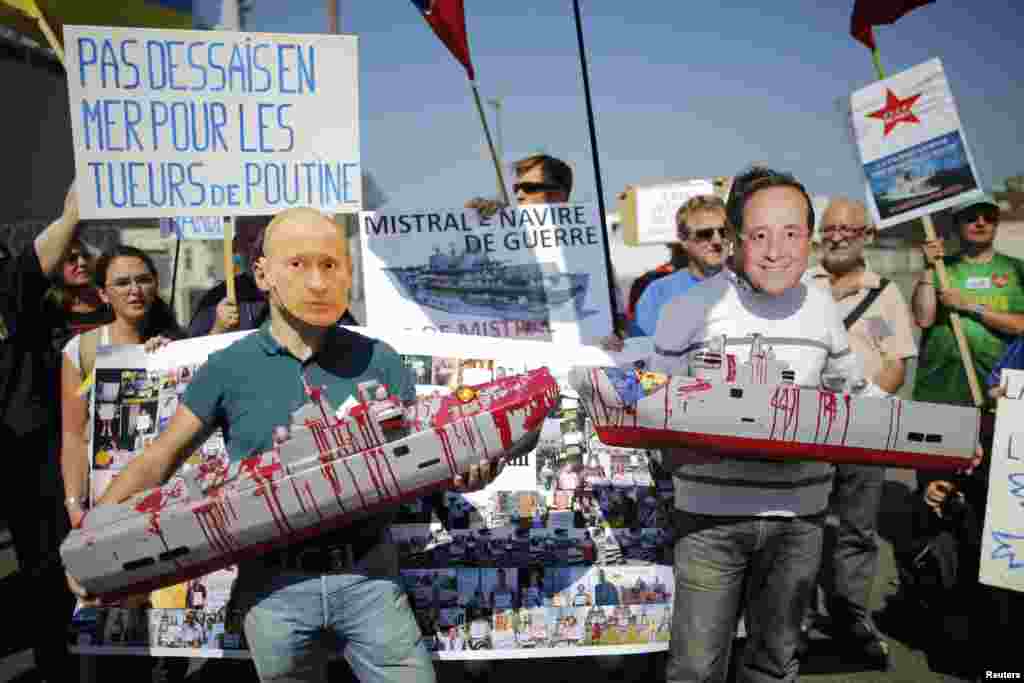 People wearing masks of French President Francois Hollande, right, and Russia's President Vladimir Putin hold up models of the Mistral-class helicopter carrier warship during a demonstration against a contract to deliver the warship to Russia, at the STX 