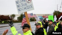 In this file photo, Boeing employees and others line the street with signs and American flags as they protest the company's coronavirus disease (COVID-19) vaccine mandate, outside the Boeing facility in Everett, Washington, October 15, 2021. (REUTERS/Lindsey Wasson) 