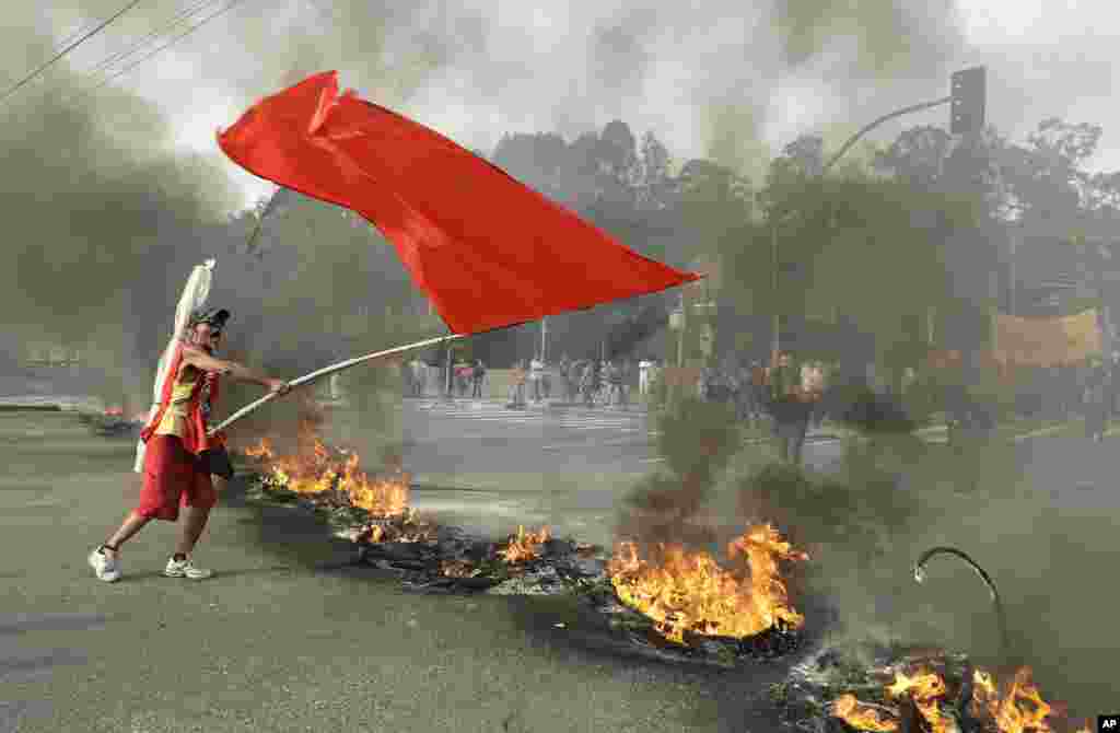 A demonstrator waves a red banner next to a burning barricade during a protest against Brazil's acting President Michel Temer, in Sao Paulo, Brazil