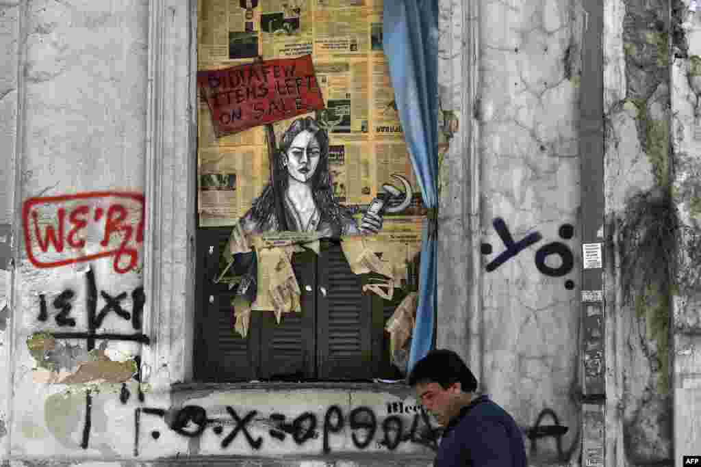 A man walks past political graffiti reading "Bid! a few items left on sale" by artist Bleeps, in central Athens, one day after Greece and its creditors closed a troubled chapter on fiscal reforms with a preliminary deal on pension and tax cuts.