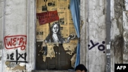 A man walks past a political graffiti in central Athens by artist Bleeps reading' Bid! a few items left on sale', May 4, 2017, one day after Greece and its creditors closed a troubled chapter on fiscal reforms.