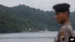 An Indonesian police stands guard in Cilacap, Central Java, Indonesia as a ferry, center background, with Indonesian police armored vehicles carrying two Australian prisoners arrives at Nusakambangan island, Wednesday, March 4, 2015.