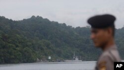 An Indonesian police stands guard in Cilacap, Central Java, Indonesia as a ferry, center background, with Indonesian police armored vehicles carrying two Australian prisoners arrives at Nusakambangan island, Wednesday, March 4, 2015.